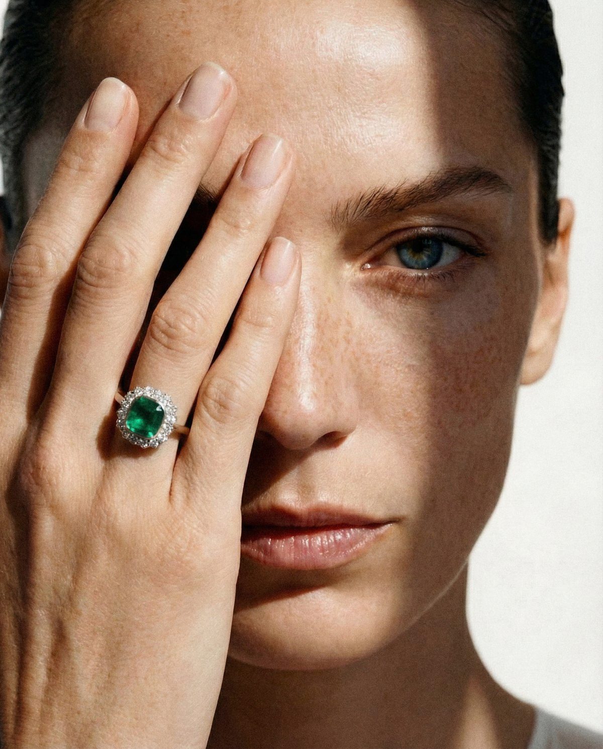 AI-directed EVARAE emerald ring, held over the face