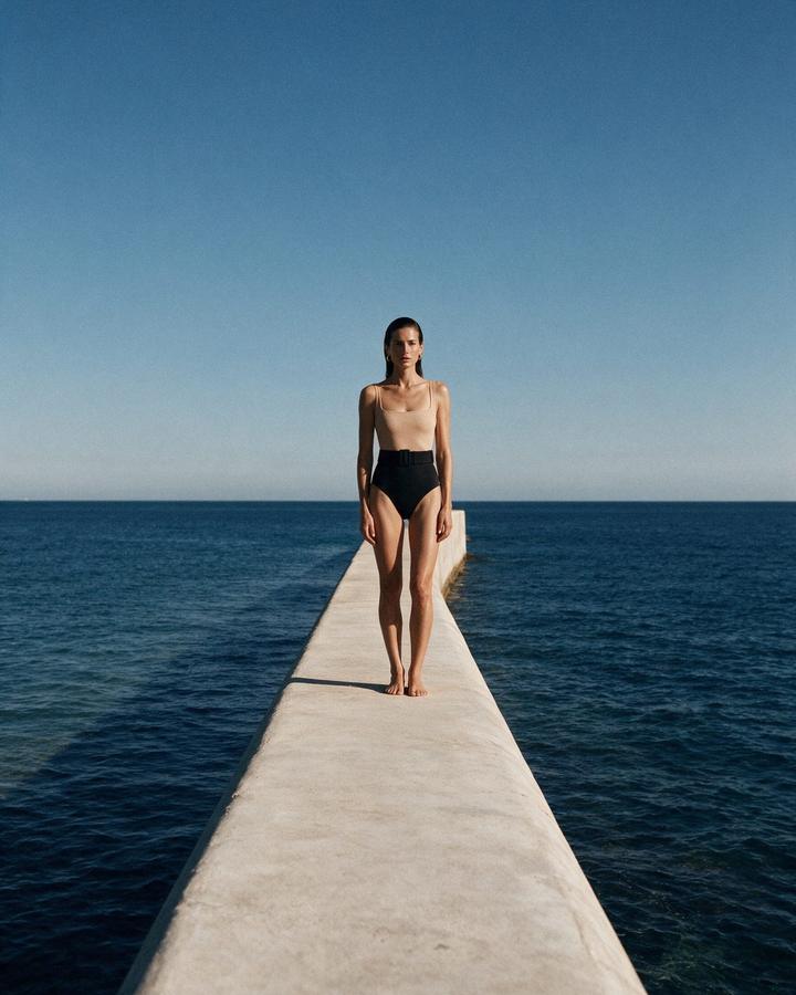 Model in the belted maillot walking the sea wall, open sea either side